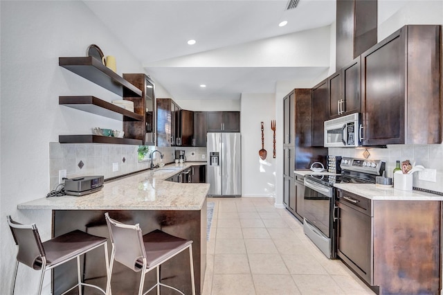 kitchen featuring light tile patterned floors, vaulted ceiling, stainless steel appliances, a kitchen bar, and open shelves