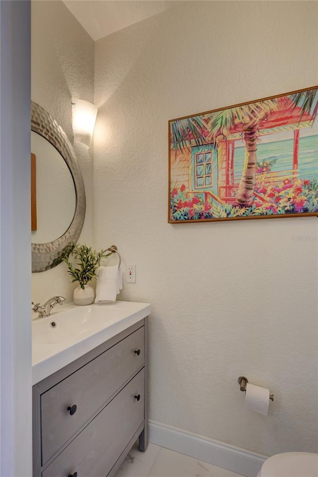 half bath with marble finish floor, vanity, and baseboards