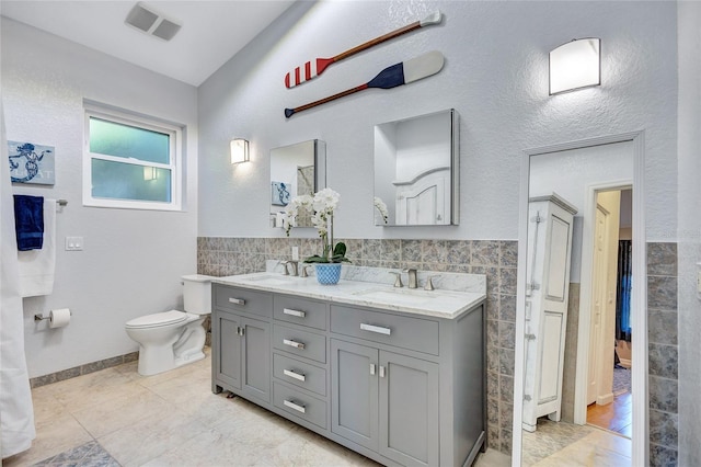 full bath with visible vents, double vanity, a sink, and tile walls