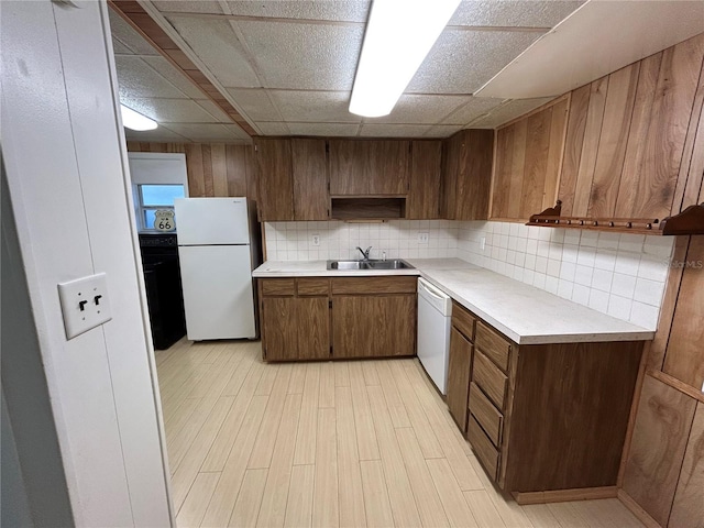 kitchen featuring light countertops, backsplash, a sink, white appliances, and a drop ceiling