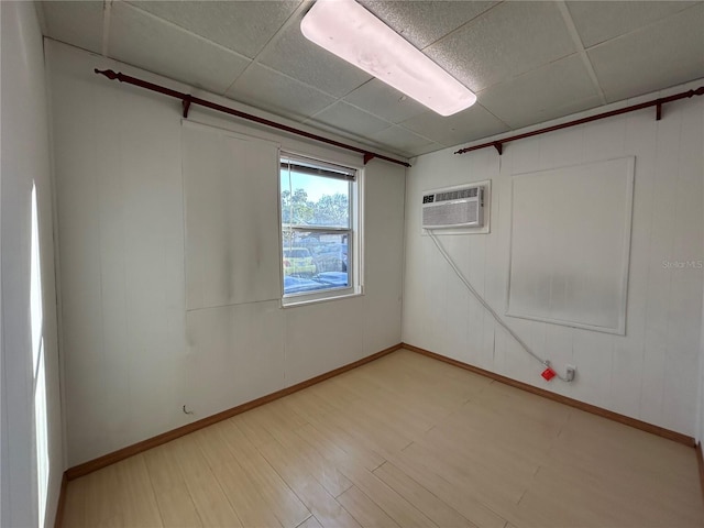 spare room with a paneled ceiling, a wall mounted air conditioner, baseboards, and wood finished floors