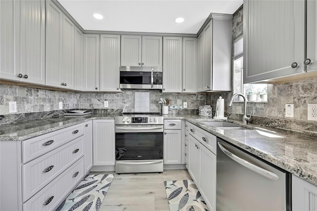 kitchen with gray cabinetry, stainless steel appliances, sink, stone counters, and decorative backsplash