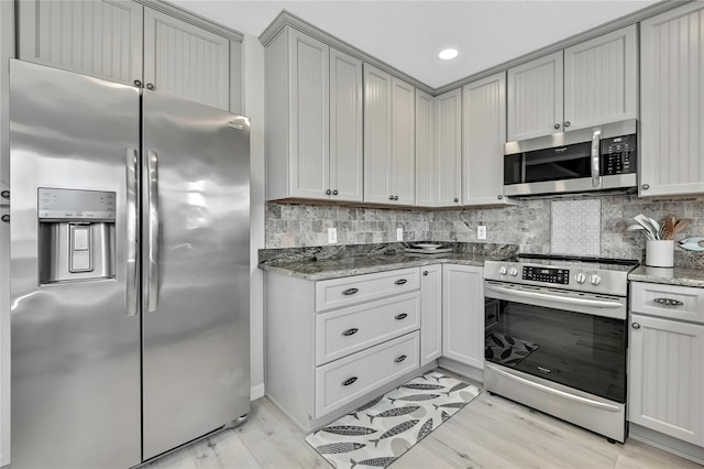 kitchen featuring light wood-type flooring, appliances with stainless steel finishes, dark stone counters, and decorative backsplash