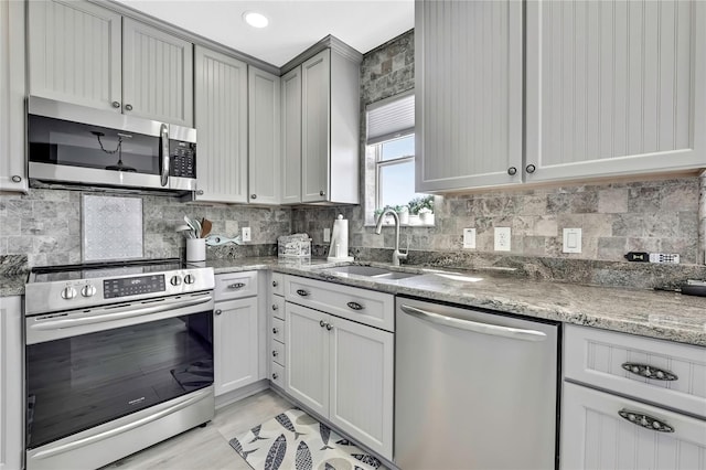 kitchen with tasteful backsplash, gray cabinetry, stainless steel appliances, dark stone counters, and sink