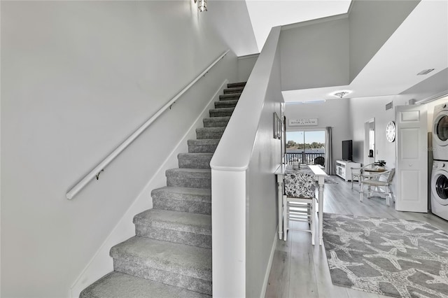 stairs with a high ceiling, hardwood / wood-style flooring, and stacked washer and dryer