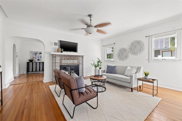 living room with arched walkways, a fireplace, wood finished floors, and a wealth of natural light