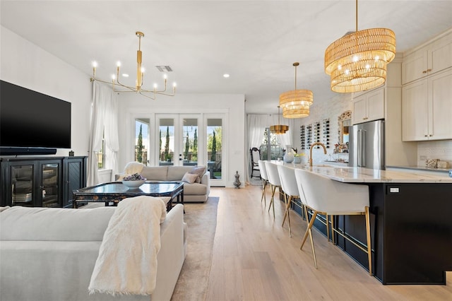 living room with light wood-type flooring, french doors, visible vents, and an inviting chandelier