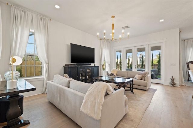 living room featuring light wood finished floors, plenty of natural light, visible vents, and a notable chandelier