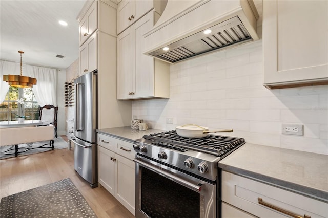 kitchen featuring tasteful backsplash, light wood-style flooring, stainless steel appliances, premium range hood, and pendant lighting