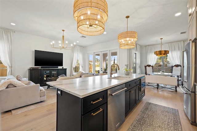 kitchen with stainless steel appliances, hanging light fixtures, open floor plan, a kitchen island with sink, and a sink