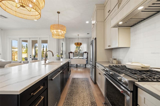 kitchen with high end appliances, decorative light fixtures, dark cabinetry, premium range hood, and a sink