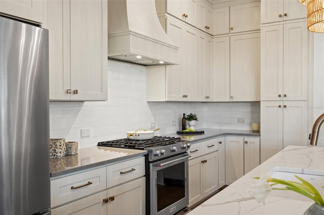 kitchen featuring tasteful backsplash, appliances with stainless steel finishes, white cabinets, light stone countertops, and premium range hood