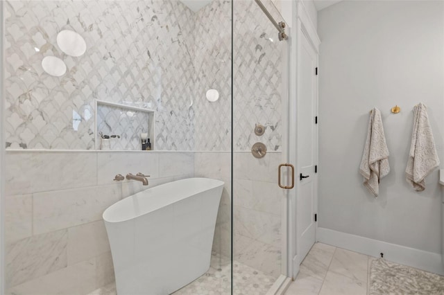 full bath featuring a stall shower, marble finish floor, a freestanding tub, and baseboards