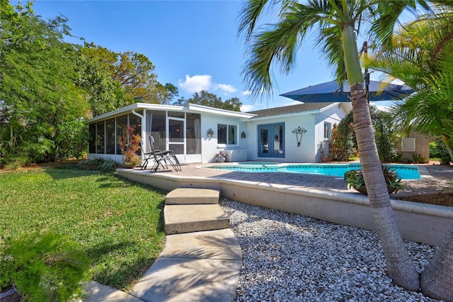 rear view of house featuring a sunroom, a yard, an outdoor pool, and french doors