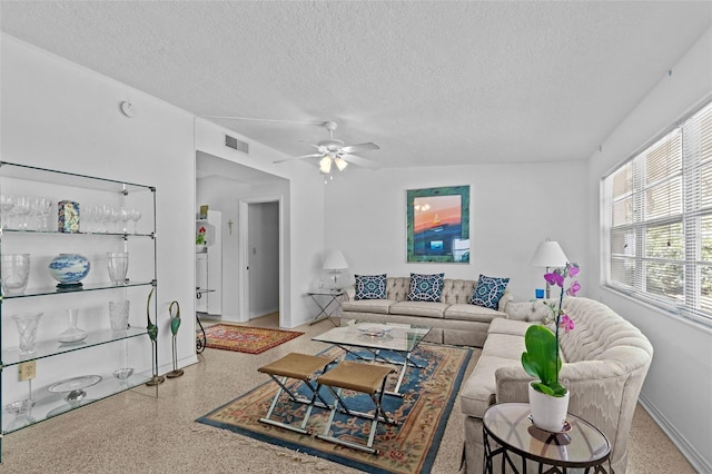 living area with a textured ceiling, speckled floor, visible vents, baseboards, and a ceiling fan