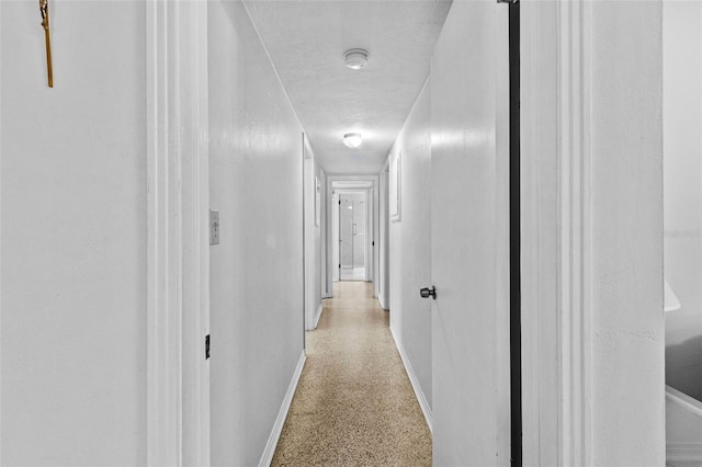 hallway with light speckled floor, a textured ceiling, and baseboards