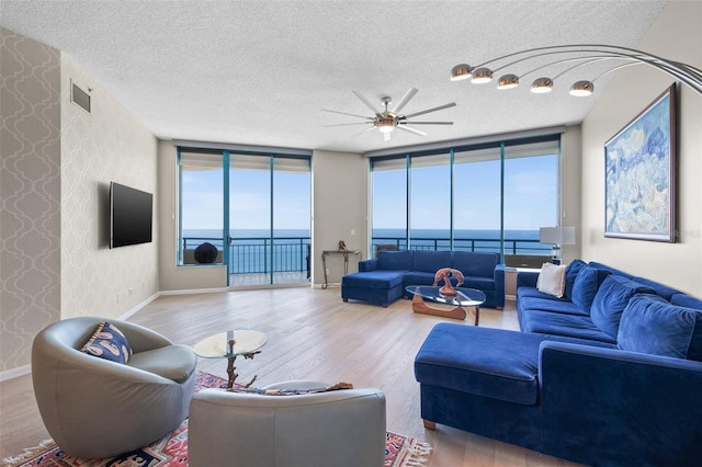 living room with a wall of windows, a textured ceiling, ceiling fan, and light wood-type flooring