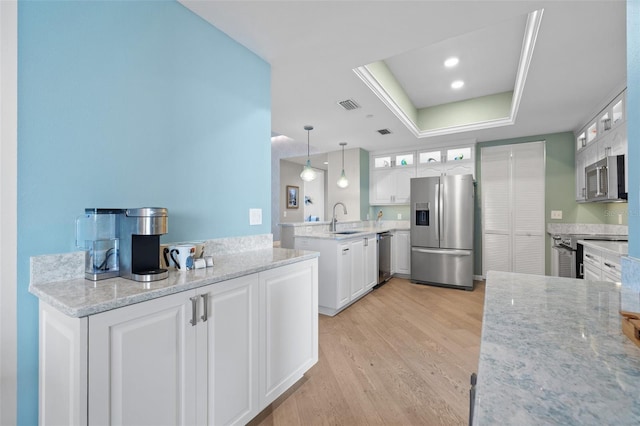 kitchen featuring appliances with stainless steel finishes, decorative light fixtures, white cabinetry, a raised ceiling, and sink