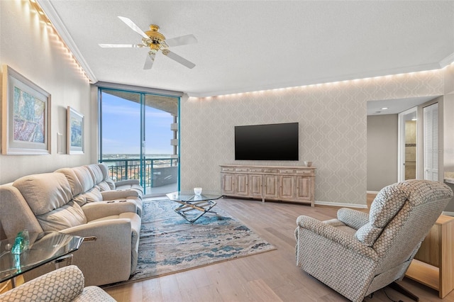 living room with ornamental molding, a textured ceiling, ceiling fan, and light wood-type flooring