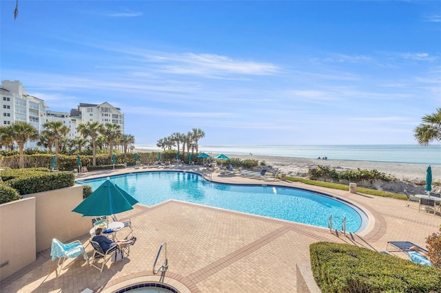 view of pool featuring a patio area, a water view, and a view of the beach