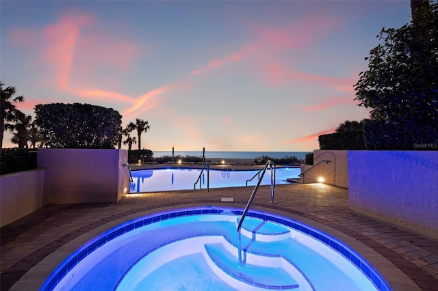 pool at dusk with a water view, a community hot tub, and a patio