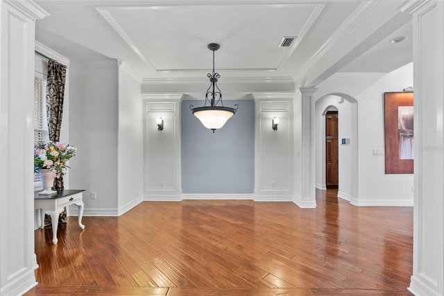 interior space featuring baseboards, visible vents, arched walkways, ornamental molding, and wood finished floors