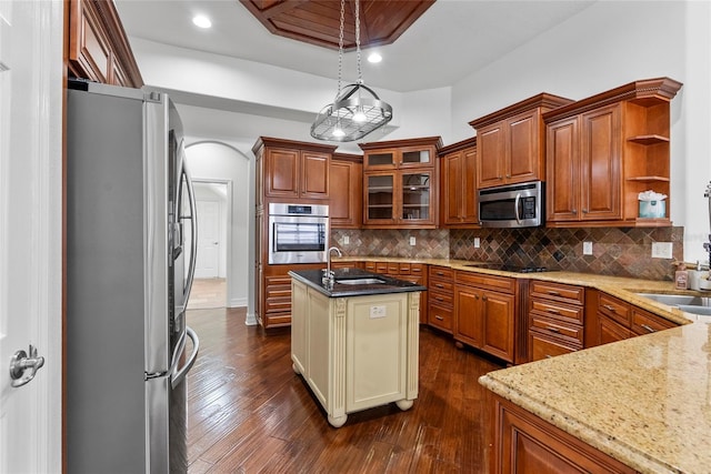 kitchen featuring decorative backsplash, appliances with stainless steel finishes, brown cabinets, light stone counters, and a sink