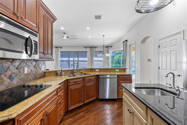 kitchen with light stone counters, arched walkways, stainless steel appliances, and a sink