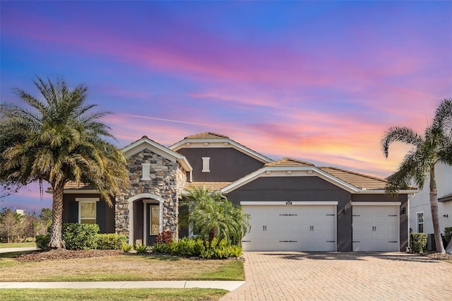 view of front of home featuring decorative driveway, stone siding, an attached garage, and stucco siding