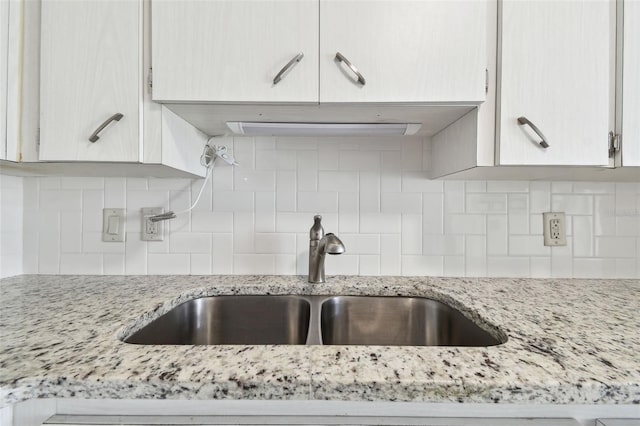 kitchen featuring a sink, backsplash, and light stone countertops