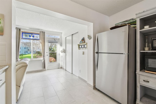 kitchen with light countertops, freestanding refrigerator, light tile patterned flooring, a textured ceiling, and baseboards