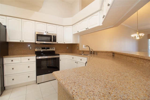 kitchen with stainless steel appliances, a peninsula, a sink, white cabinets, and decorative light fixtures