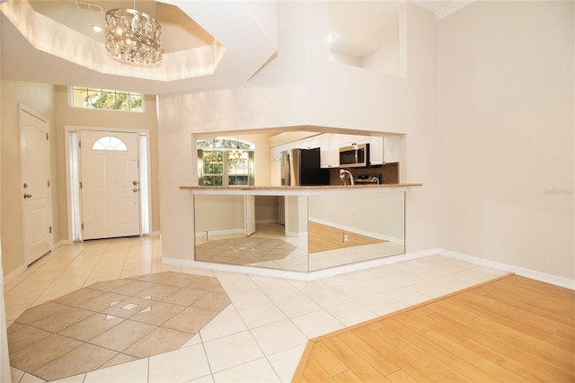 entrance foyer with baseboards, a raised ceiling, an inviting chandelier, a high ceiling, and light tile patterned flooring