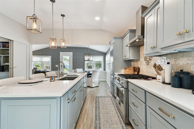 kitchen with high end stainless steel range, lofted ceiling, gray cabinets, wall chimney exhaust hood, and a sink