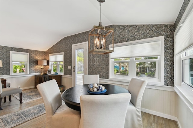 dining area featuring a wainscoted wall, a notable chandelier, wood finished floors, wallpapered walls, and vaulted ceiling