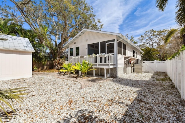 back of house with a gate, an outbuilding, a fenced backyard, and a sunroom