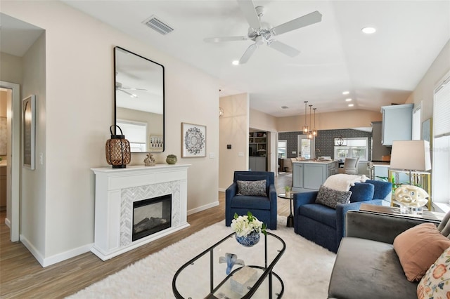 living area with visible vents, vaulted ceiling, a fireplace, and light wood finished floors