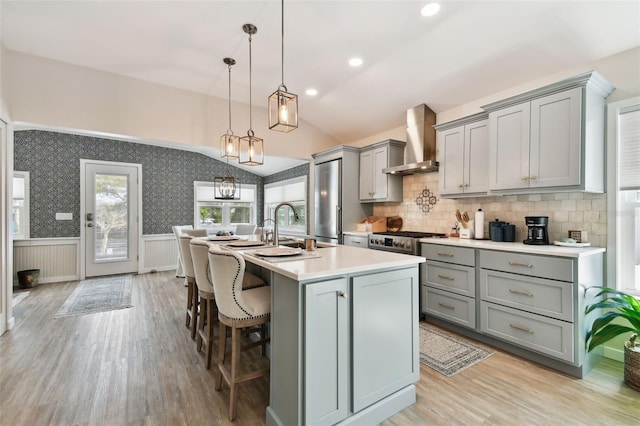 kitchen with gray cabinets, vaulted ceiling, light countertops, wainscoting, and wall chimney range hood