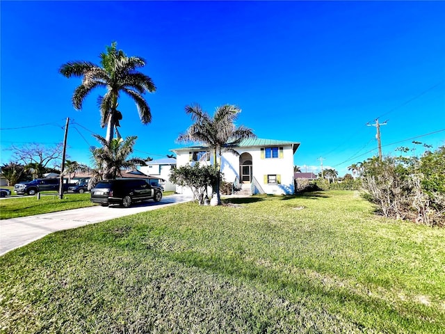 view of front facade featuring stucco siding, driveway, metal roof, and a front lawn