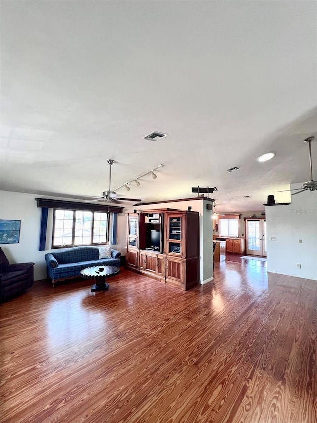 unfurnished living room with plenty of natural light, visible vents, dark wood-style flooring, and ceiling fan