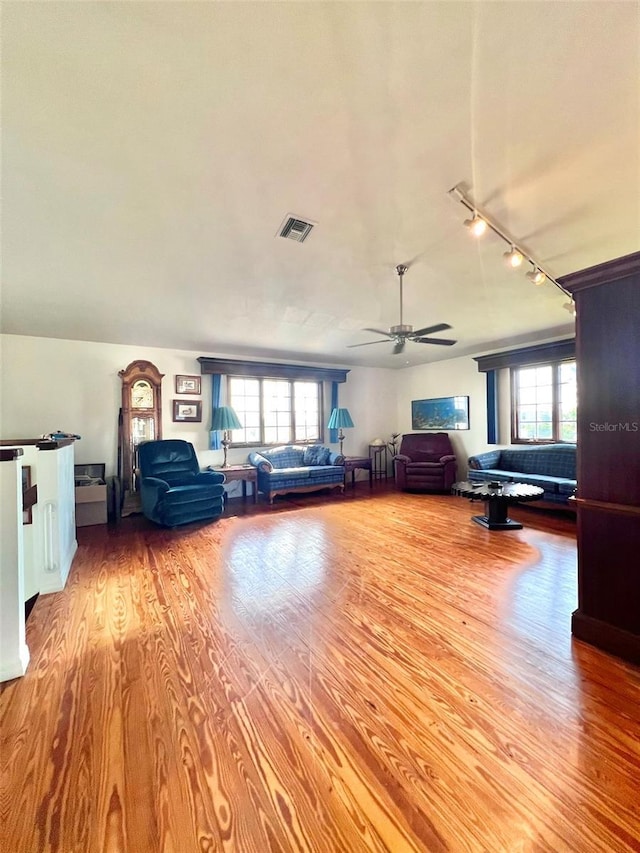 unfurnished living room with a ceiling fan, plenty of natural light, wood finished floors, and visible vents