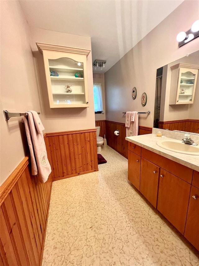 bathroom featuring vanity, wood walls, wainscoting, tile patterned floors, and toilet