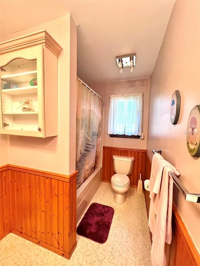 bathroom with shower / bath combo with shower curtain, toilet, wood walls, and wainscoting