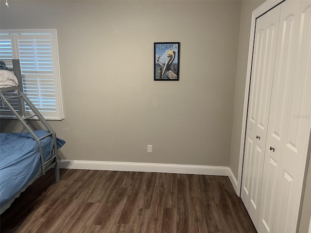 unfurnished bedroom featuring a closet, dark wood finished floors, and baseboards