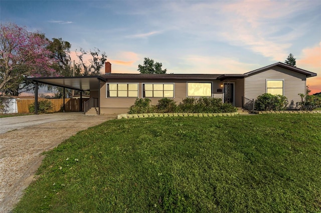 view of front of home with a lawn, an attached carport, driveway, and fence