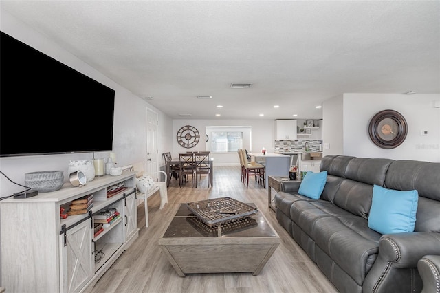 living area with light wood finished floors, recessed lighting, a textured ceiling, and visible vents