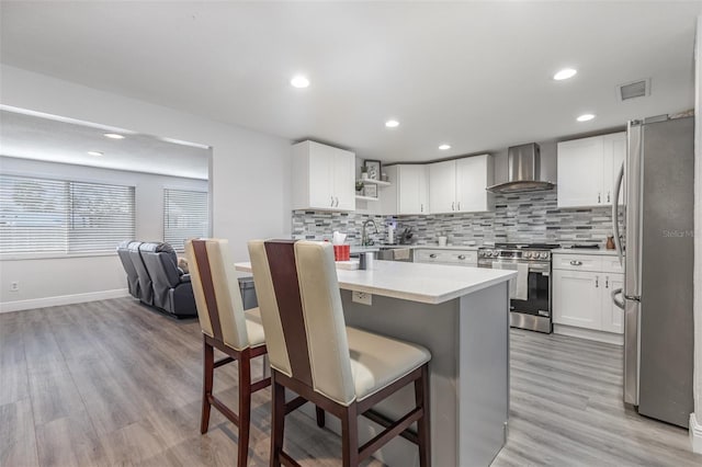 kitchen with white cabinets, light countertops, appliances with stainless steel finishes, wall chimney range hood, and a kitchen breakfast bar