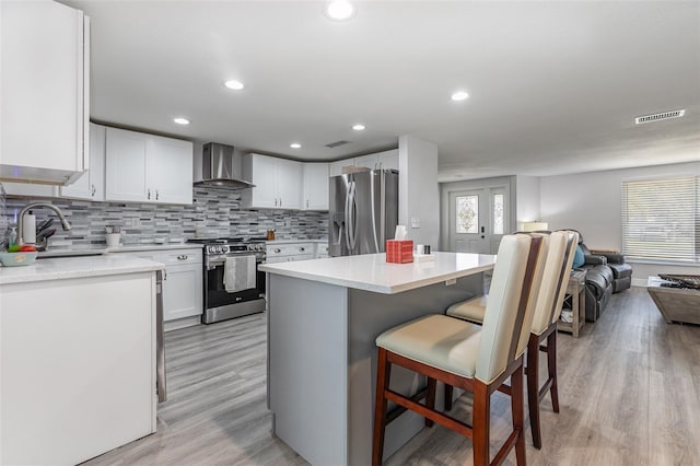 kitchen with open floor plan, white cabinetry, a sink, stainless steel appliances, and wall chimney range hood