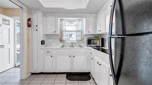 kitchen featuring light tile patterned floors, tasteful backsplash, freestanding refrigerator, and white cabinetry