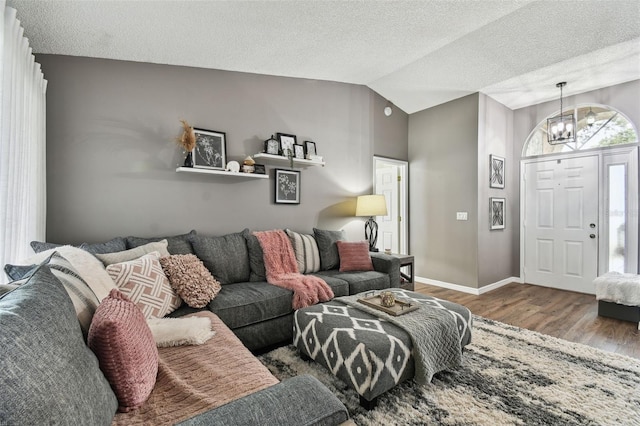 living room with a textured ceiling, hardwood / wood-style flooring, an inviting chandelier, and lofted ceiling